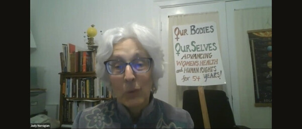 A screenshot of Judy from the event. She is sitting in front of a book shelf and a sign that reads "Our Bodies Ourselves." She has short white hair and is wearing glasses. Below in black is the following text: "Our Bodies Ourselves: Half a Century of Health & Sexuality Education and Activism"