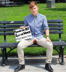 A trans and non-binary person sitting on a bench bleeding through their pants as they hold a sign that says, "Periods are not just for women. #BleedingWhileTrans."