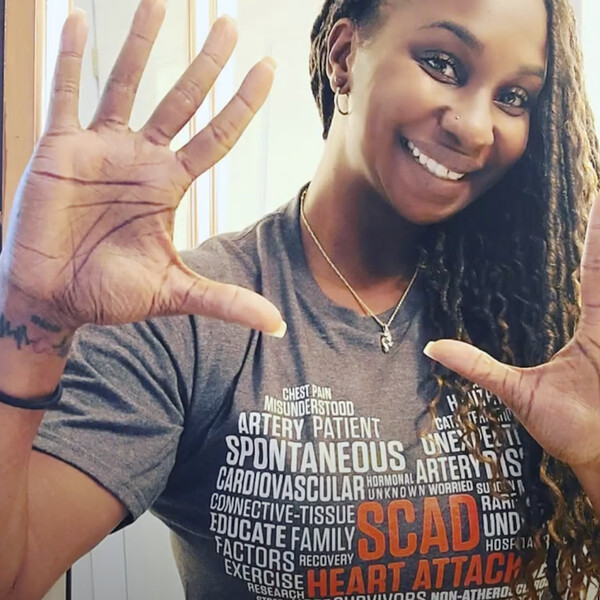 A woman in a heart attack t-shirt holds up both hands