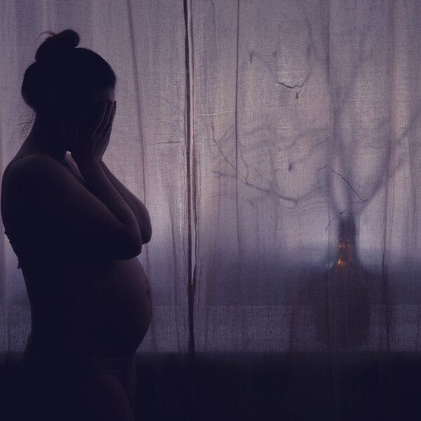 A sad pregnant woman in front of a dark curtain