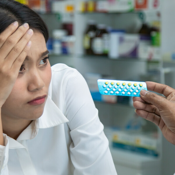 An Asian woman looks concerned as a pharmacist hands her birth control pills
