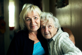 An elderly mother and her older adult daughter pose for a picture together