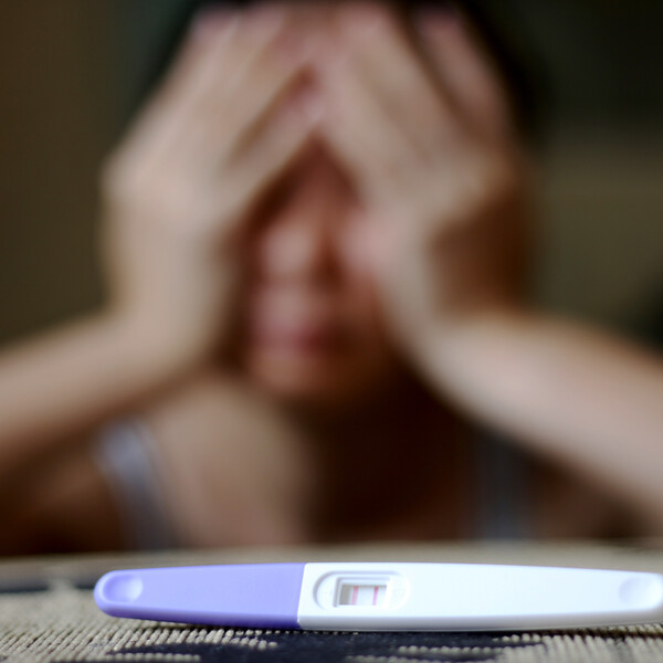 A woman has her hands on her head as though disappointed. In front of her is a positive pregnancy test on a table.