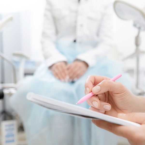 A woman sits in a gynecological office as a doctor takes notes