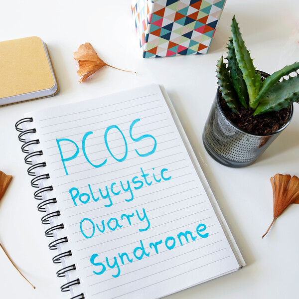 A notebook on a white table with the words "PCOS Polycystic Ovary Syndrome" written on it