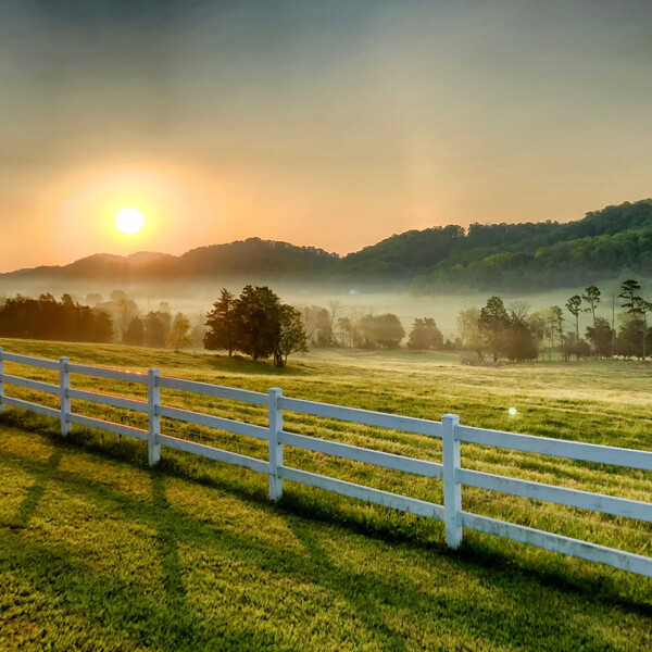 Sun rising over the mountains in the distance, with a white picket fence extending diagonally in the foreground
