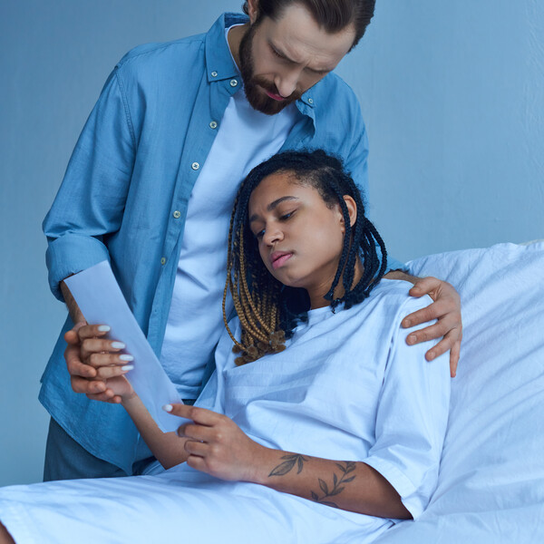 sad man standing near african american wife, looking at ultrasound, hospital, miscarriage concept