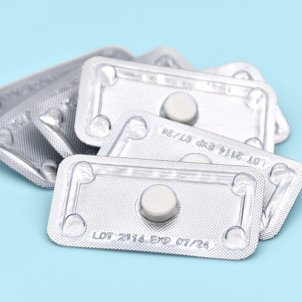 A blue background with a few packs of individual white emergency contraceptive pills.