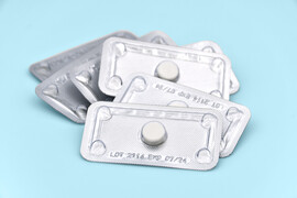 A blue background with a few packs of individual white emergency contraceptive pills.