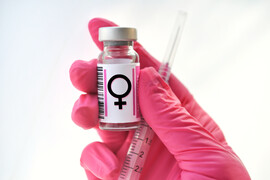 A white background. A hand with a pink glove holding a vial and needle with the female symbol.