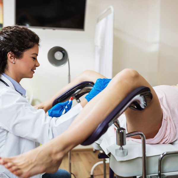 A doctor sits in front of a pregnant woman patient with her legs open and in stirrups. The patient is wearing a pink hospital gown.
