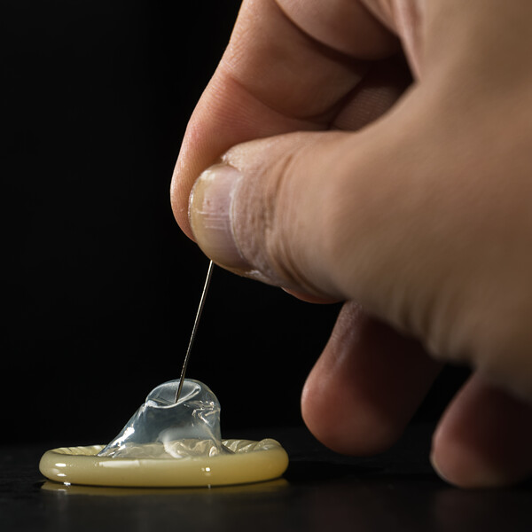 A hand holding a needle that is pricking a condom