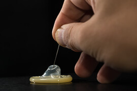 A hand holding a needle that is pricking a condom