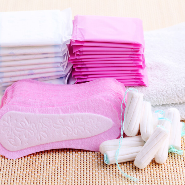 A stack of pink pads next to a stack of white pads. Next to them are white towels. In front of those stacks are pink panty liners and white tampons.