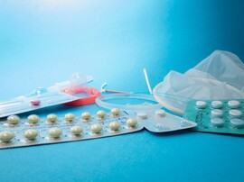 A blue table with a stack on birth control items including internal and external condoms, the implant, a copper IUD, the ring, a vial for injection, and different pills