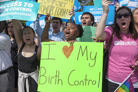 People at a protest for birth control. Centered is a Black woman shouting and holding a lime green sign that reads: "I love (heart) my birth control." To her left is an Asian woman in a black tank top shouting and holding a sign that reads: "Access to Birth Control NotMYBossBusiness." To the right of the Black woman is a white woman in a pink Planned Parenthood t-shirt who is also shouting. She has a sign in one hand and a rainbow/LGBTQ+ flag in the other.