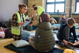 A woman volunteer in a yellow vest speaks with a woman at a shelter