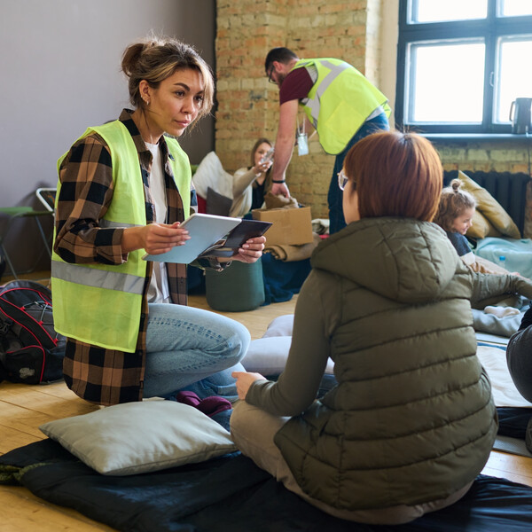 A woman volunteer in a yellow vest speaks with a woman at a shelter