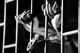 A black and white photo of handcuffed hands holding prison bars