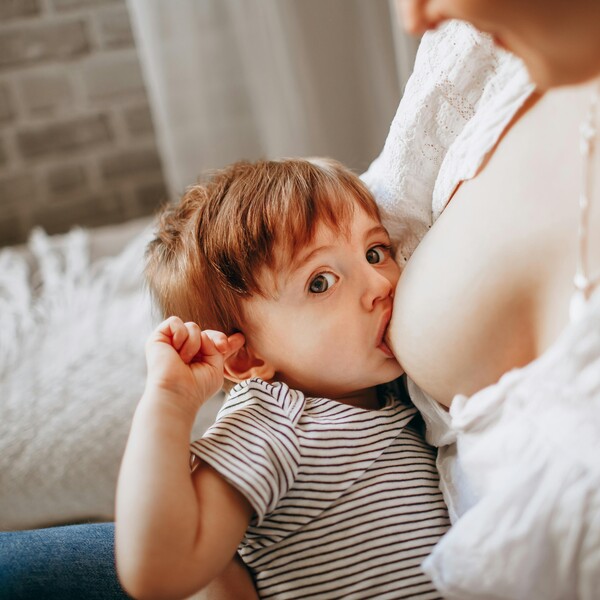 A woman breastfeeds a baby who looks at the camera