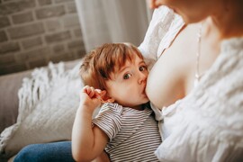 A woman breastfeeds a baby who looks at the camera