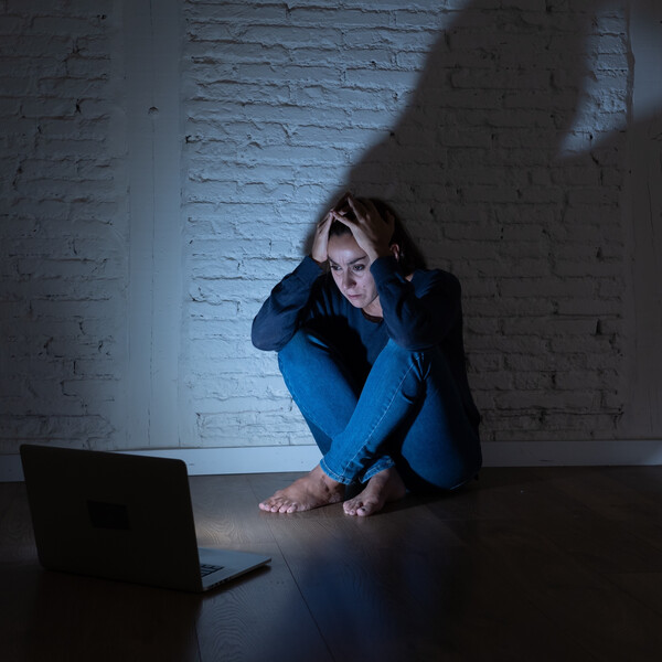 A woman sits across from an open laptop looking scared and concerned