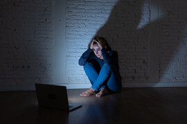 A woman sits across from an open laptop looking scared and concerned