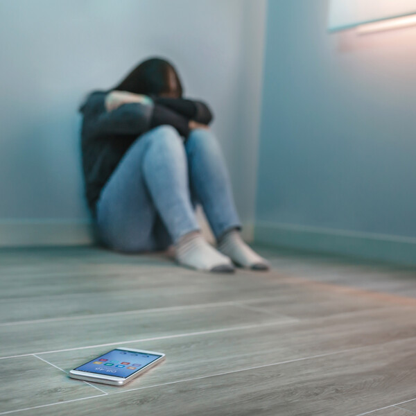 A woman sits balled up in a corner away from her phone