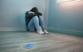 A woman sits balled up in a corner away from her phone