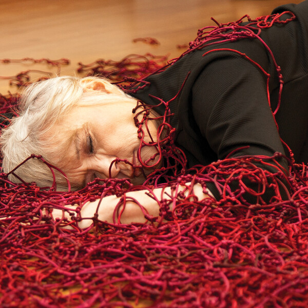 A woman lays on the floor surrounded by red knots