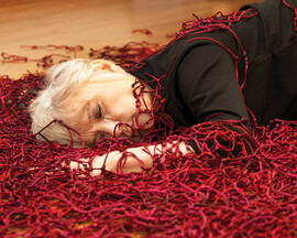 A woman lays on the floor surrounded by red knots