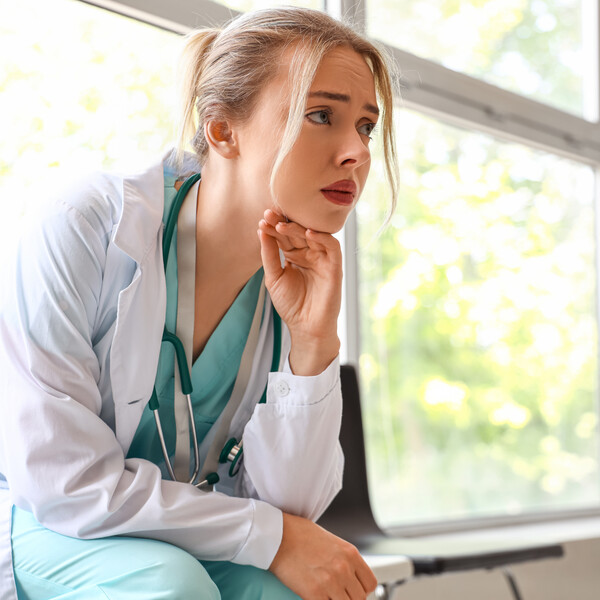 A woman doctor sits on a bench looking concerned