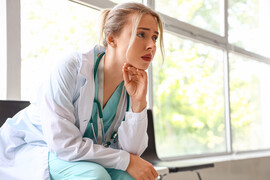 A woman doctor sits on a bench looking concerned