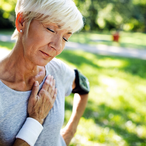 A close up of an older woman standing outside holds her hand over her chest
