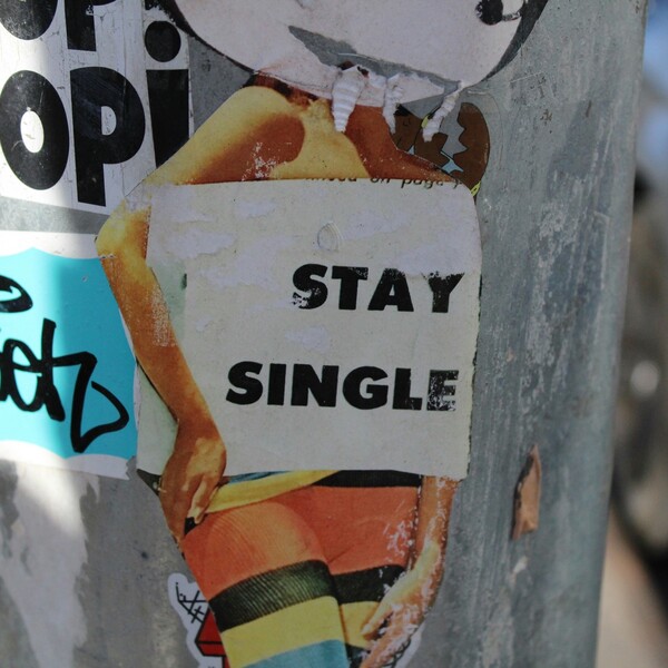 A sticker on a light pole of a woman's silhouette with a white box that reads "Stay Single"