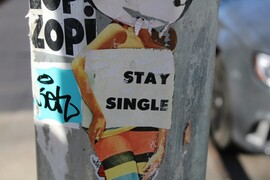 A sticker on a light pole of a woman's silhouette with a white box that reads "Stay Single"
