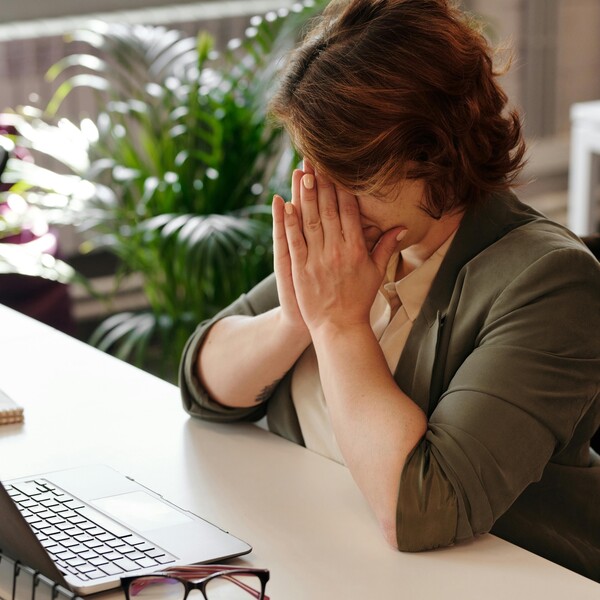A woman in a wheelchair sits at her desk with her hands on her face