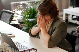 A woman in a wheelchair sits at her desk with her hands on her face