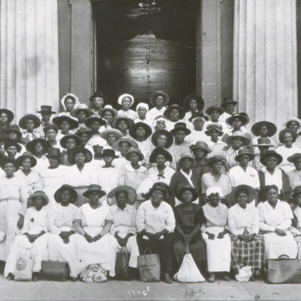 A large group of Black women midwives stand outside of a courthouse