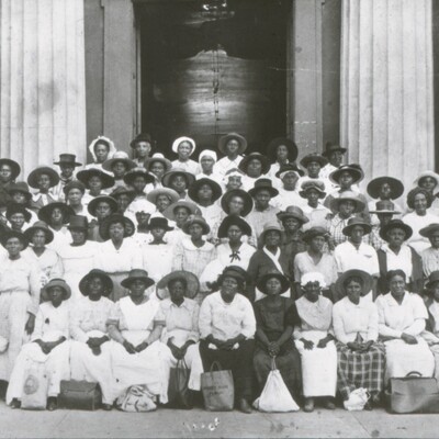 A large group of Black women midwives stand outside of a courthouse