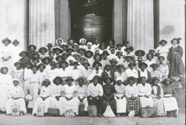 A large group of Black women midwives stand outside of a courthouse