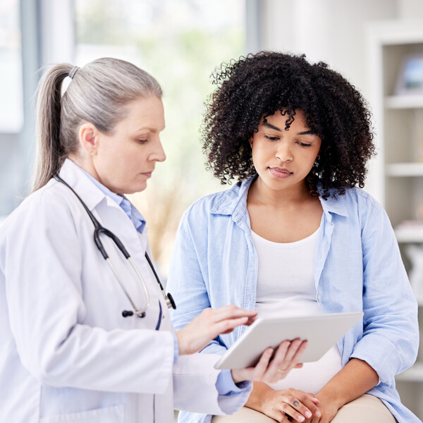 A pregnant woman looks at a tablet with a doctor