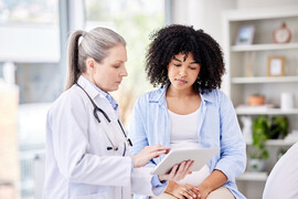 A pregnant woman looks at a tablet with a doctor
