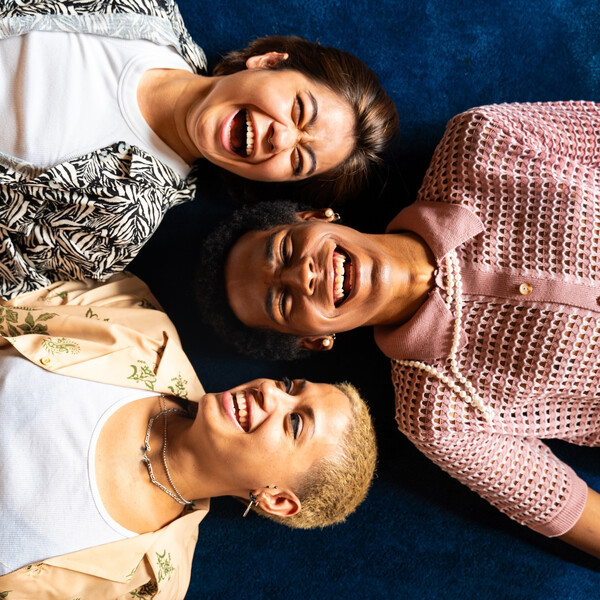 Three queer people lay on the floor laughing together