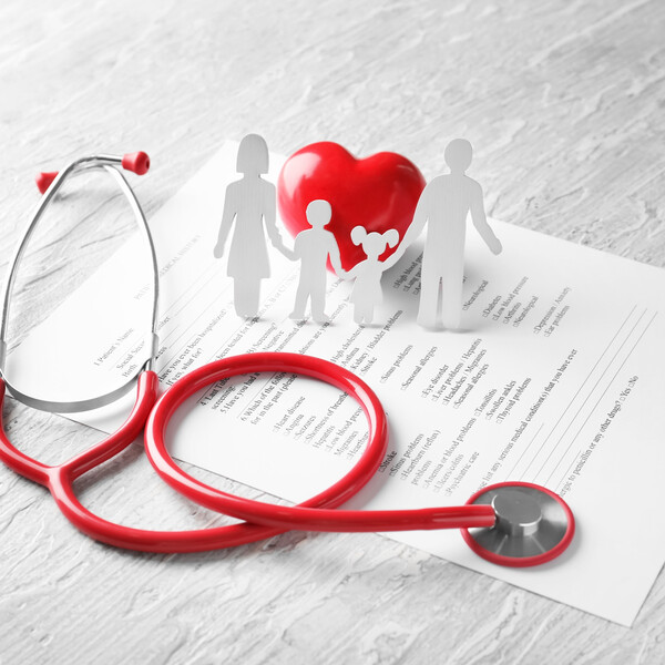 A white table with a family history form, a stethoscope, and a paper cutout of a family around a heart