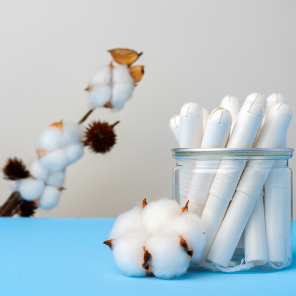 A blue table with a glass jar with tampons in it and a cotton plant in the background