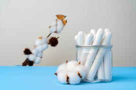 A blue table with a glass jar with tampons in it and a cotton plant in the background
