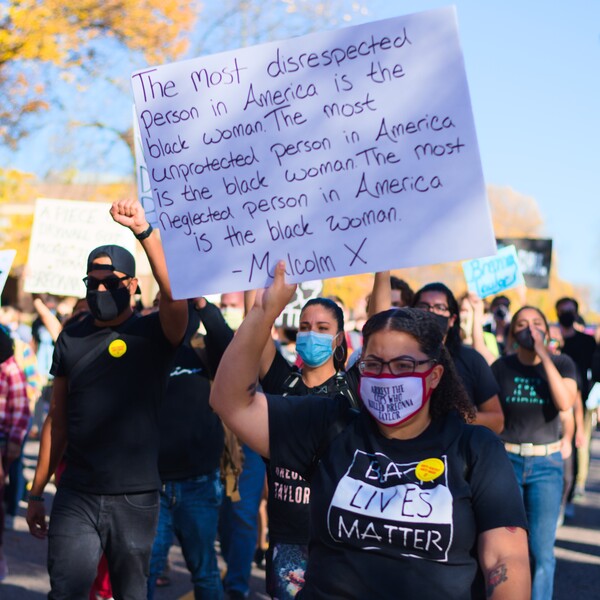 People at a Black Lives Matter march. A woman holds a sign that reads: "The most disrespected person in America is the black woman. The most unprotected person in America is the black woman. The most neglected person in America is the black woman. - Malcolm X."