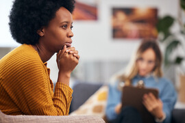 A Black woman with an afro sits in front of a therapist