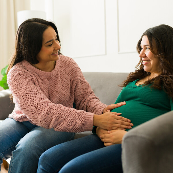 A happy pregnant woman sits on the couch being checked by her doula